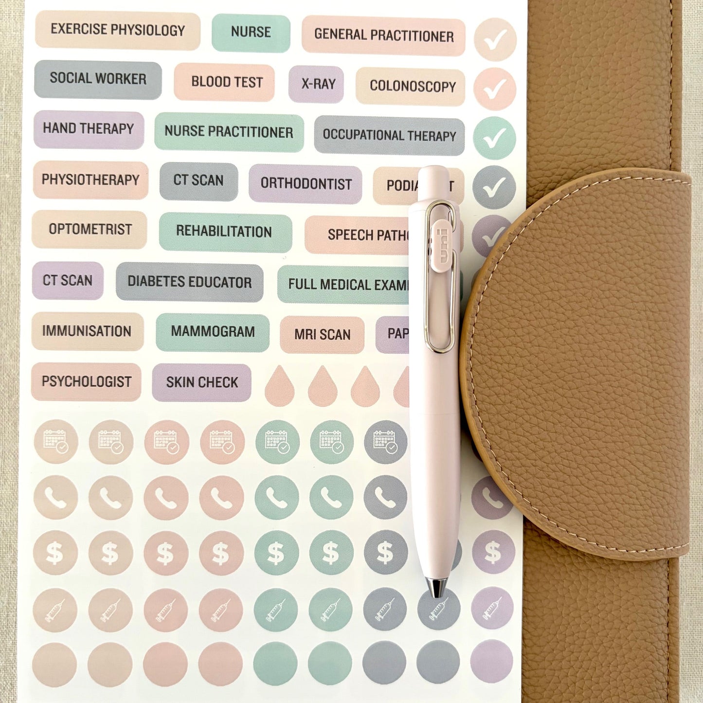 Sheet of medical and lifestyle stickers on a beige planner cover with a pen.