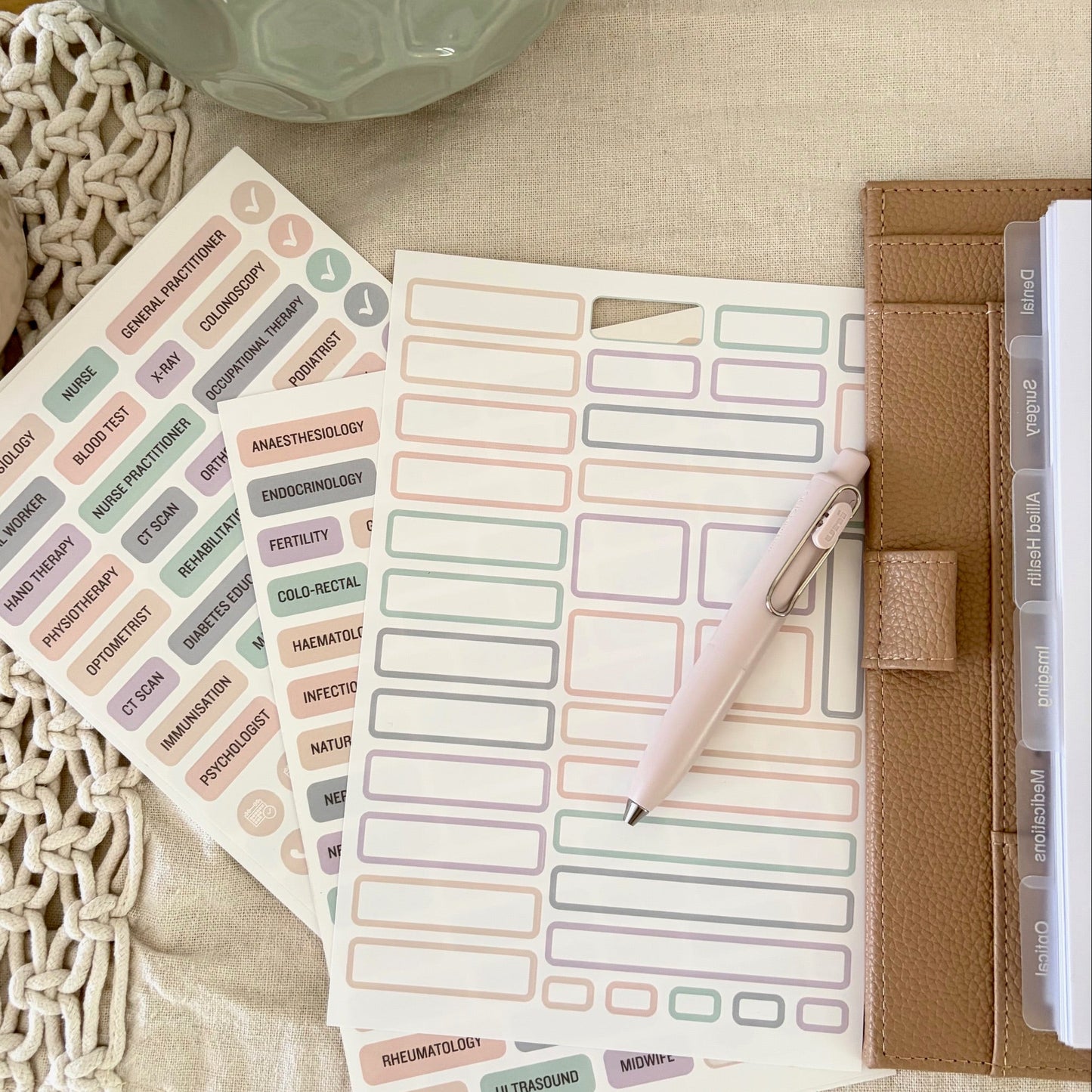 Sticker sheets and a pen on a textured surface with a decorative object in the background.